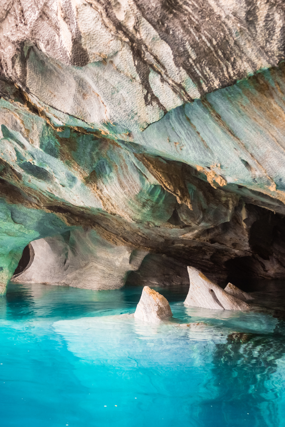 Interior view of the Marble Caves in Patagonia, showing smooth, swirling rock formations in shades of blue, gray, and white, with vibrant turquoise water reflecting the cave walls.