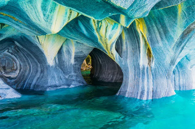 Colorful view of the Marble Caves in Patagonia, Chile, showing smooth, swirling marble formations in shades of blue, yellow, and white above clear turquoise water.