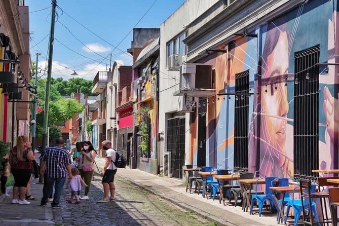 People standing talking on a cobblestone street with brightly painted cafes along the street and tables set on the side walk for people to eat at in the Palermo neighborhood in Buenos Aires, Argentina