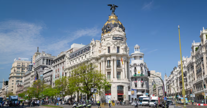 Two major streets meet at Gran Via in Madrid, where the buildings are this impressive bright white color and people are walking, shopping, and exploring..
