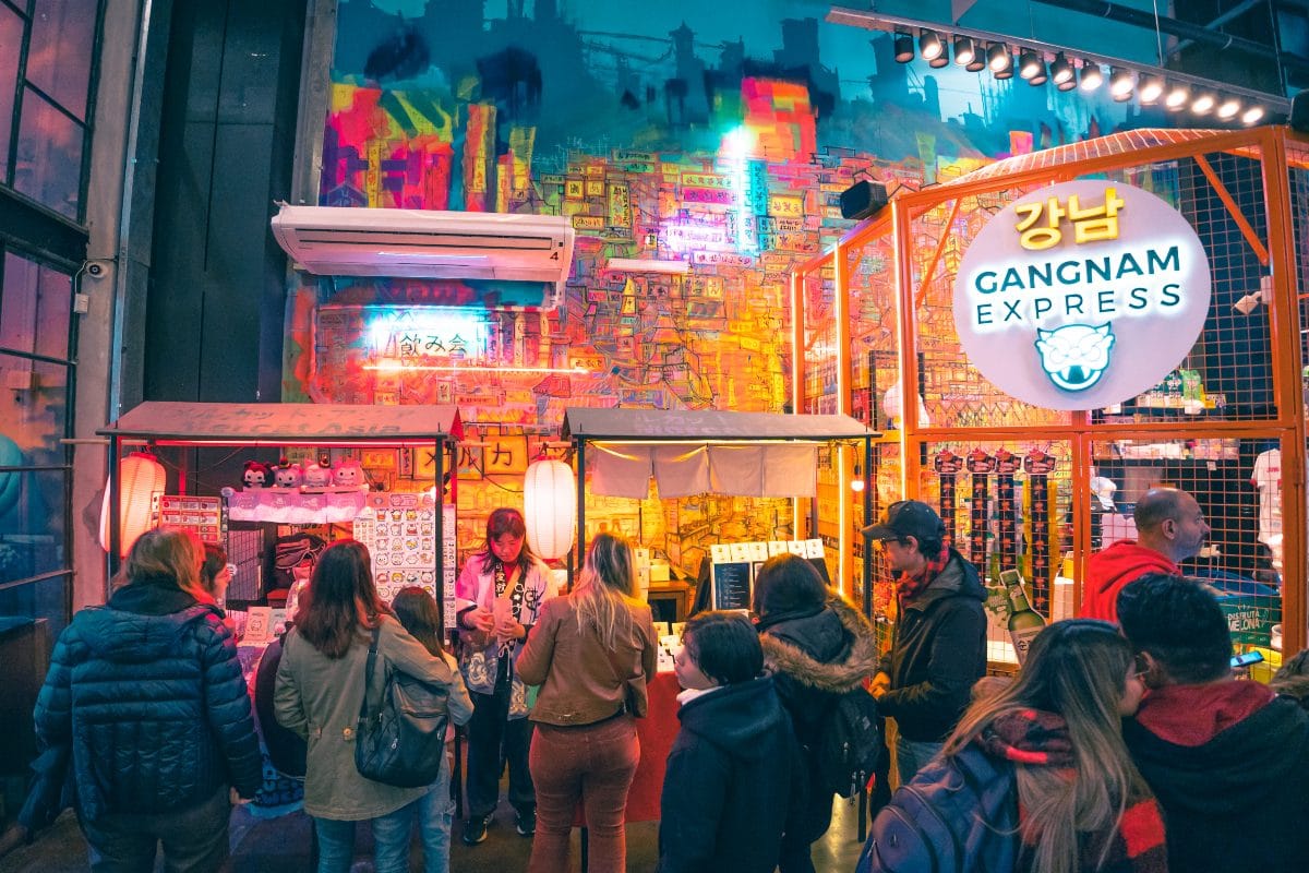 Long line of Local people waiting in line to order food from a food vendor that has a brightly lit up food cart with neon lights in the Villa Crespo Neighborhood in Buenos Aires.
