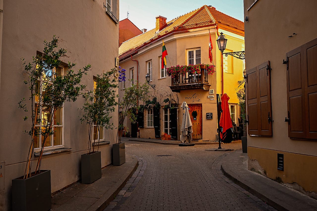  A charming cobblestone alley in Old Town Vilnius, Lithuania, lined with potted trees, historic buildings, and a cozy café.