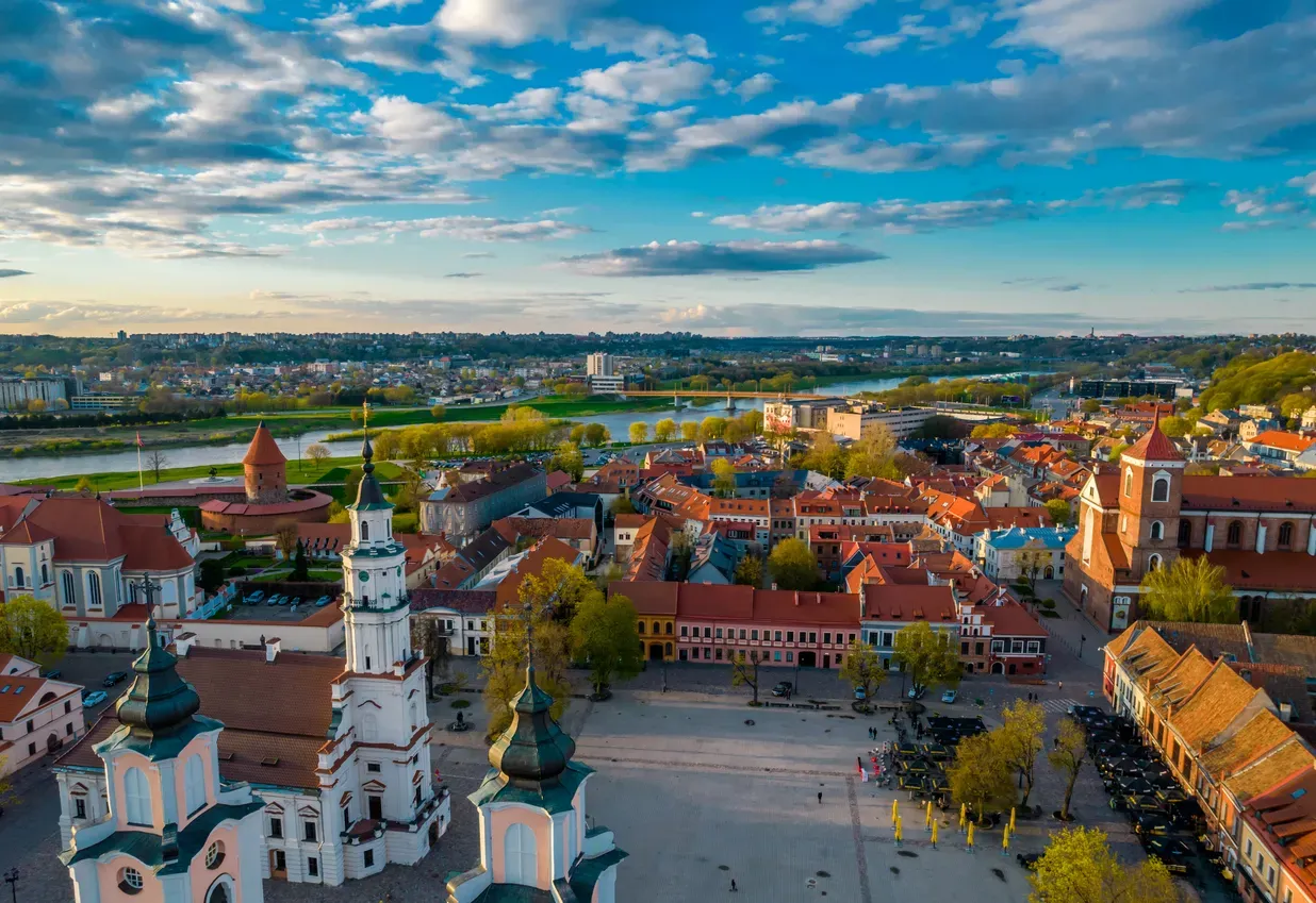 Ariel view of city buildings in Kaunas, Lithuania have red shingle roofs and the river can be seen in the distance.