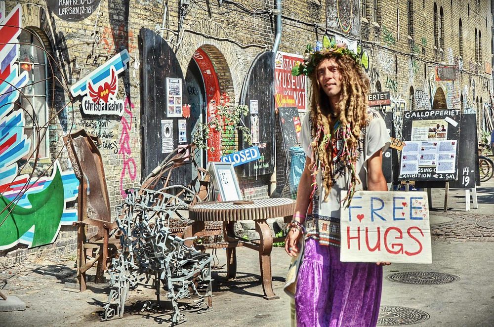 Man dressed like a hippie holding a sign that says free hugs inside of Freetown Christiania in Copenhagen, Denmark.