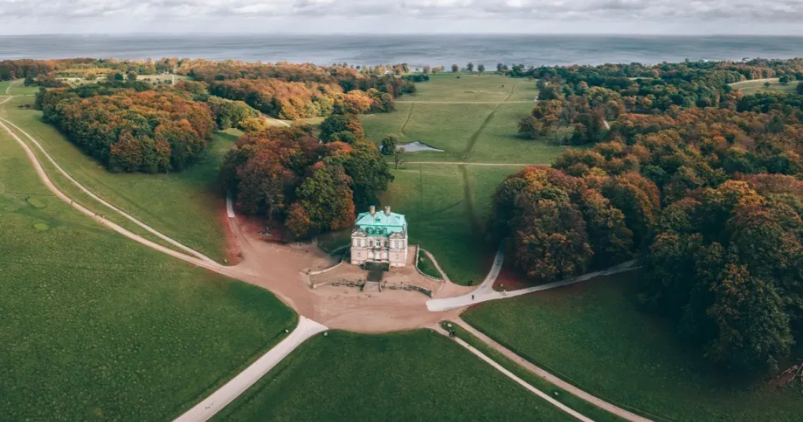 Ariel view of a large manor with beautiful forest and fields surrounding the structure at Jægersborg Dyrehave in Denmark.