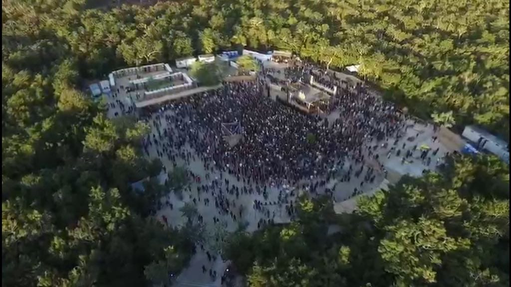 Ariel view of a crowd of people at a venue in the jungle with stages set up for DJ's to perform.