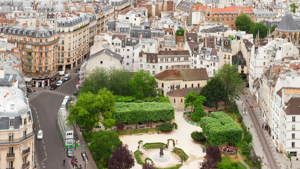 Aerial view of the Latin Quarter in Paris, featuring a historic park with a central fountain, surrounded by classic Haussmann-style buildings and narrow winding streets.