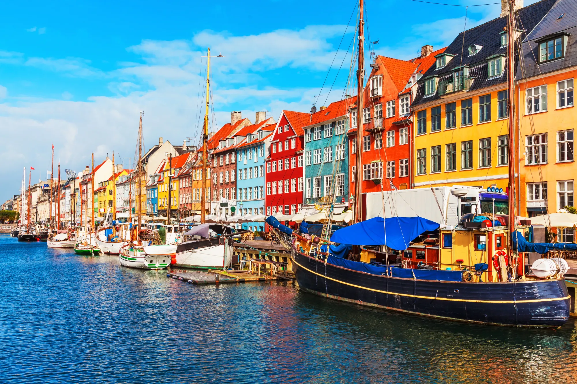 Colorful buildings line the street next to a cancal with boats sitting in the water at Nyhavn in Copenhagen, Denmark.