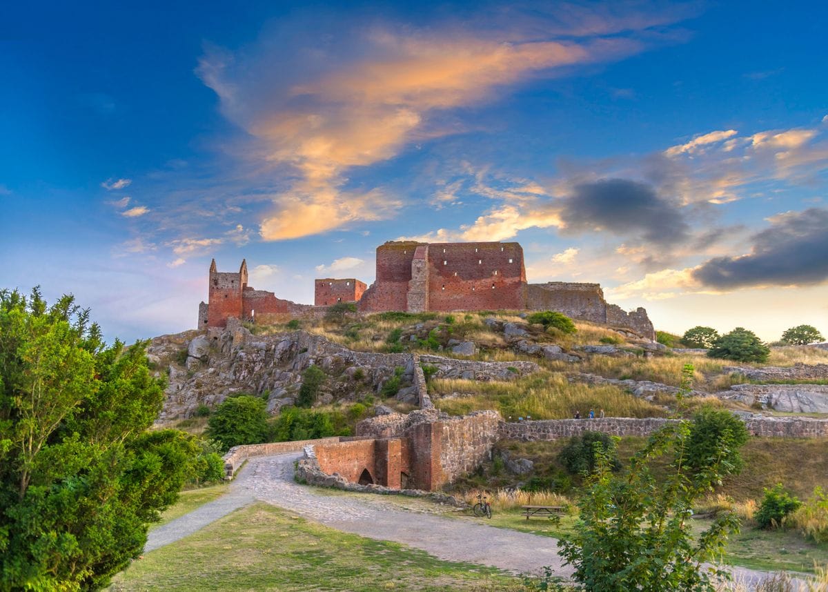 Lush green trees in front of a road that leads to large castle ruins at Bornholm’s Hammershus in Denmark.