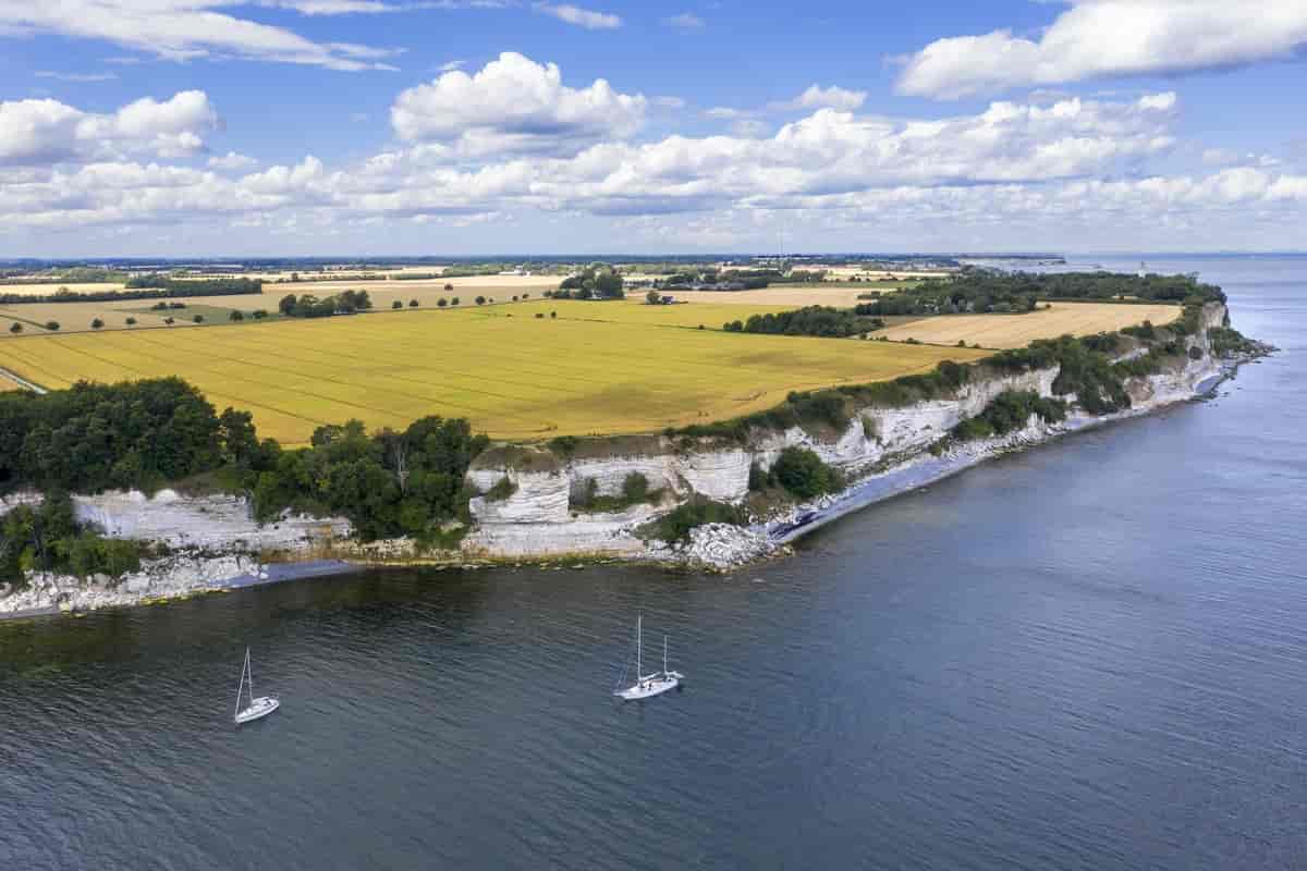 A field leading to seaside cliffs with sailboats anchored near the cliffs at Stevns Klint in Denmark.