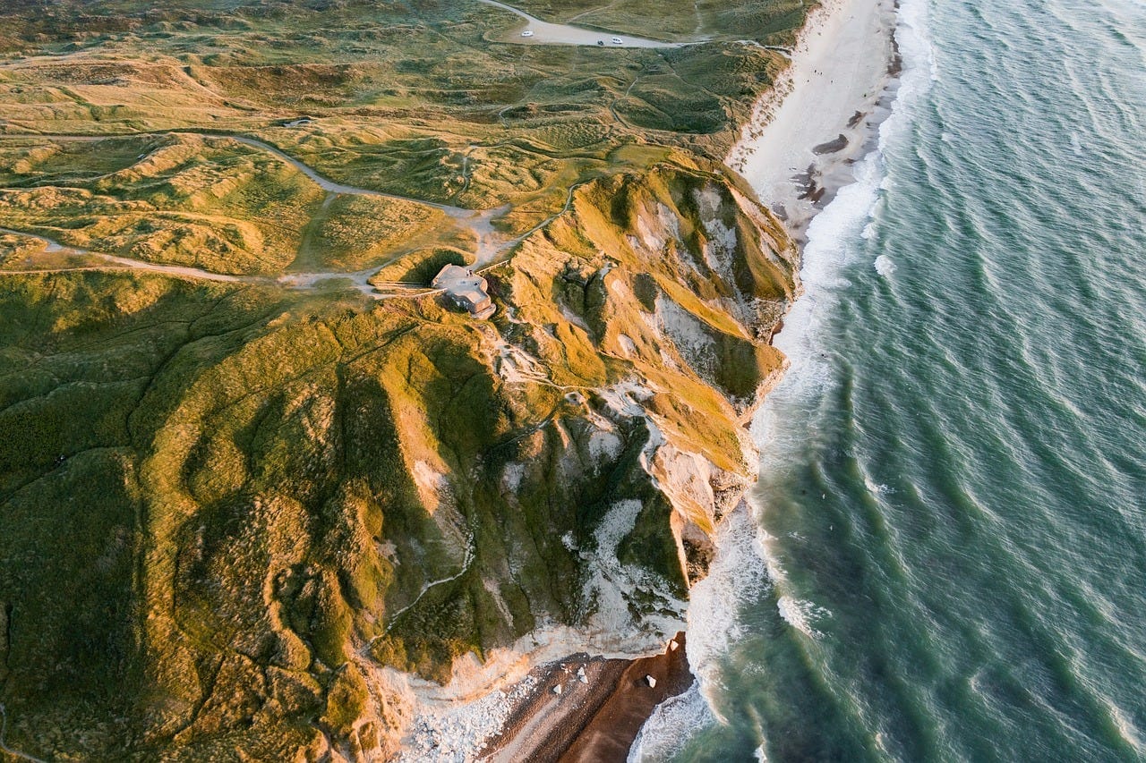 Ariel view of The Cliffs of Bulbjerg in Denmark shows jagged cliffs covered in green grass and towering over the ocean.