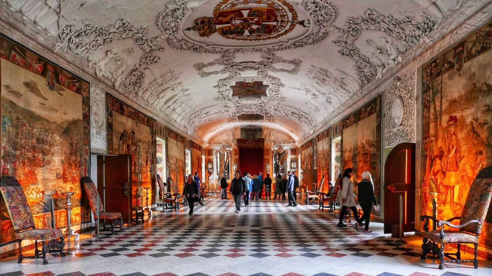 People walking through the interior of Rosenborg Castle, showing the walls covered in beautiful art.