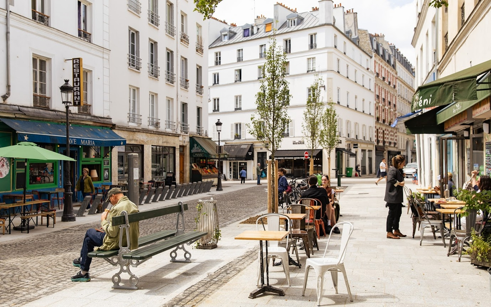 Lively daytime scene on Rue Oberkampf in Paris, France, featuring outdoor cafés, people dining and relaxing, classic Parisian architecture, and a cobblestone pedestrian-friendly street.