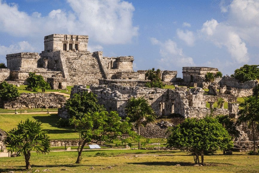 The ancient Mayan ruins of Tulum, Mexico, featuring a well-preserved stone structure known as El Castillo, perched on a grassy landscape.