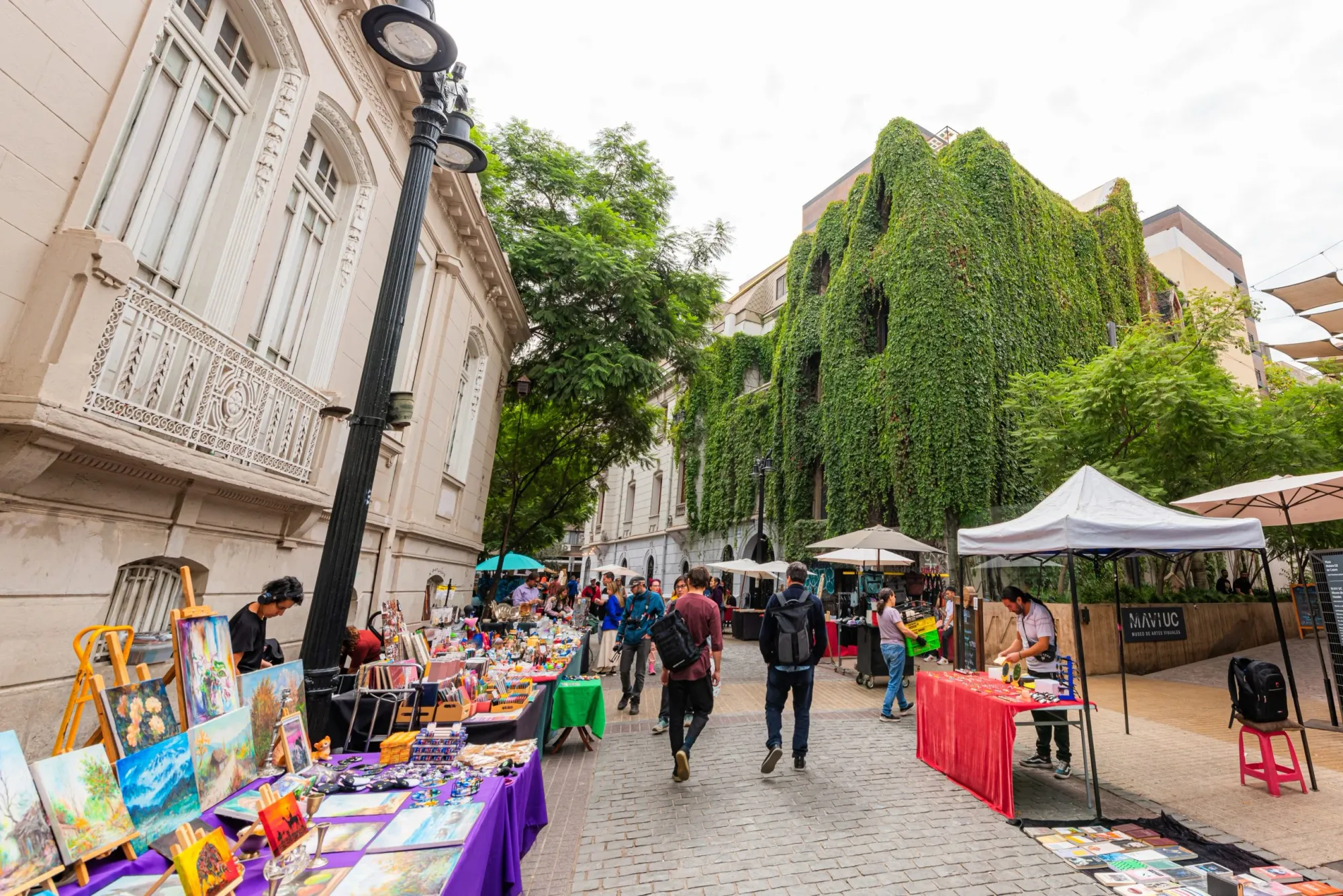 People walking the street looking at people selling arts and crafts they have displayed at their booths along the street.