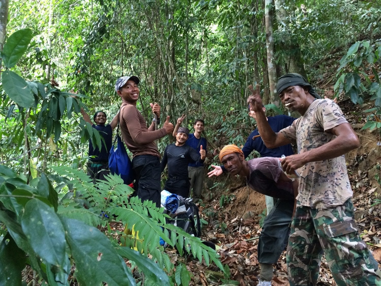 A few tourist are walking up a trail in the jungle with local Thai jungle guides.