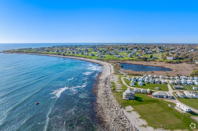 Ariel view of a rocky beach that then turns to sand and is near a subdivision. 