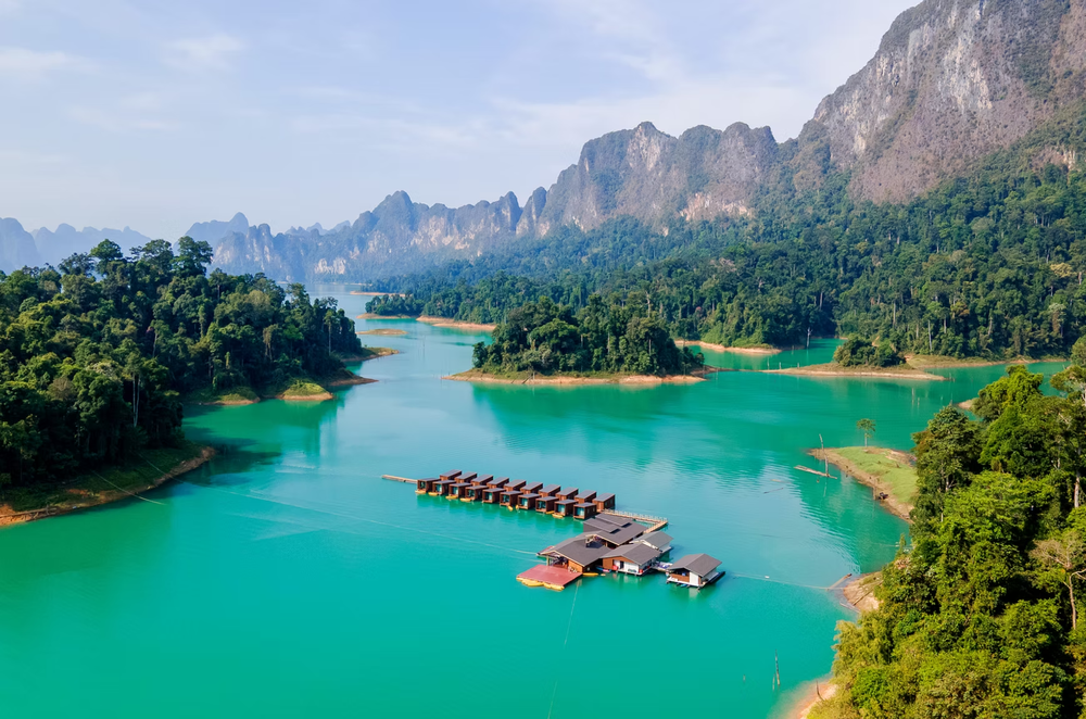 A floating resort with bungalows in emerald lake water surrounded by giant mountains and surrounded by jungle in Khao Sok National Park.