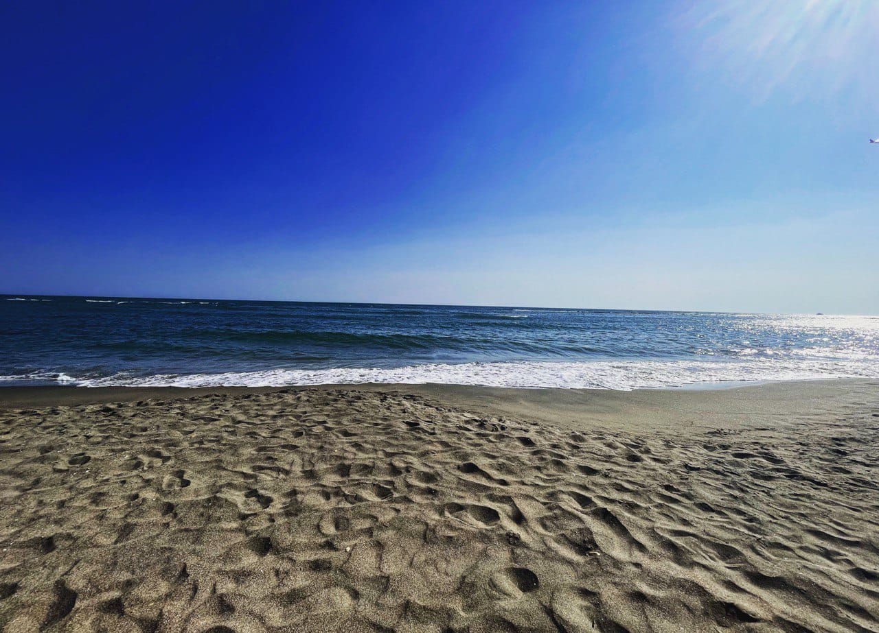 Wavey sand leading out to the waters edge with ocean as far as the eye can see with clear blue skies. 