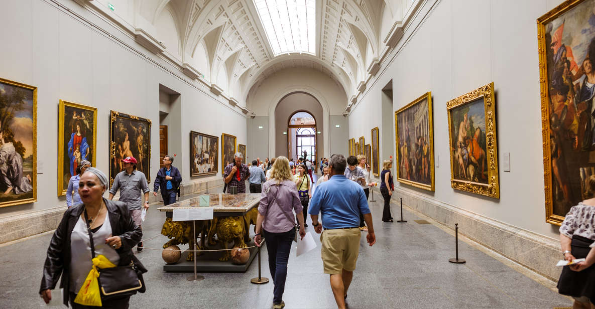 People walking in a large room at Museo del Prado with paintings on each side of the wall.