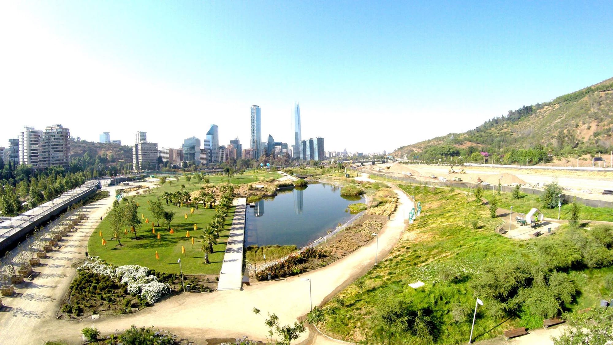 Ariel view of a park with walkways going around a body of water with the skyline of Santiago in the background.