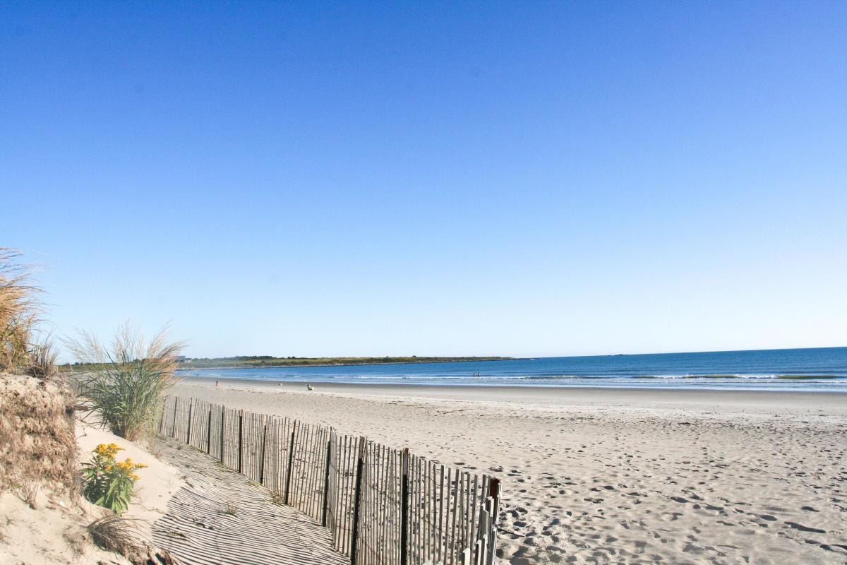 A fence along the sand dunes before the beach opens up and leads to the waters edge.