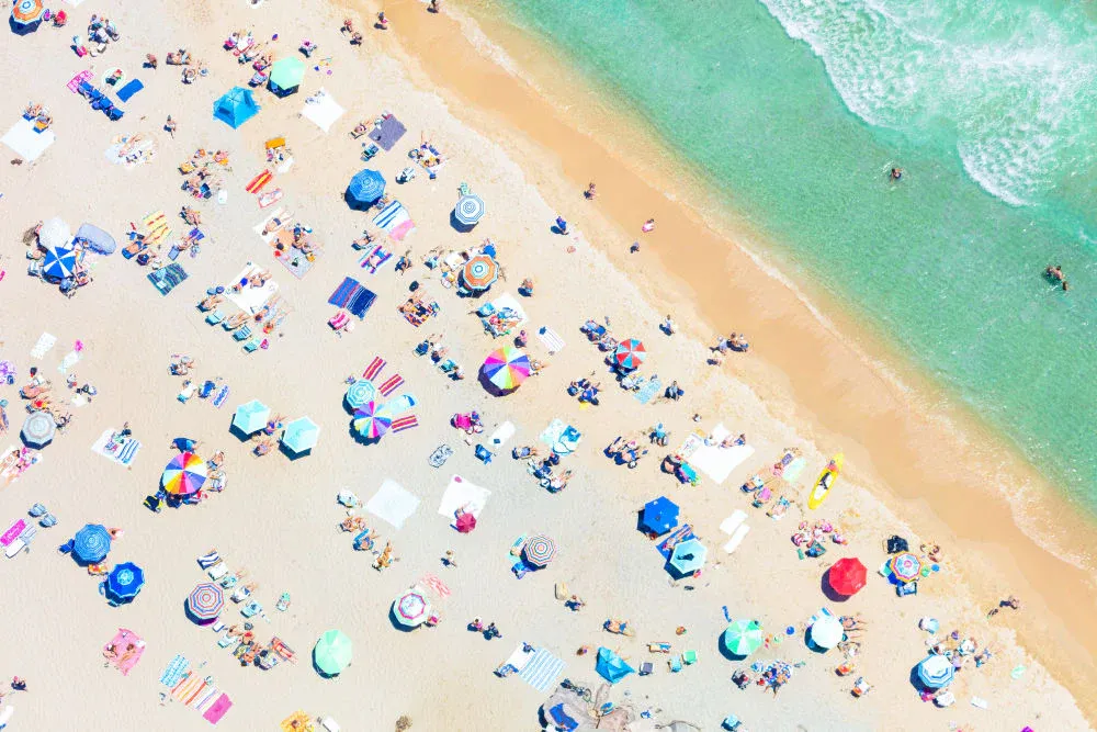 Ariel view of people laying on a beach with colorful umbrellas.