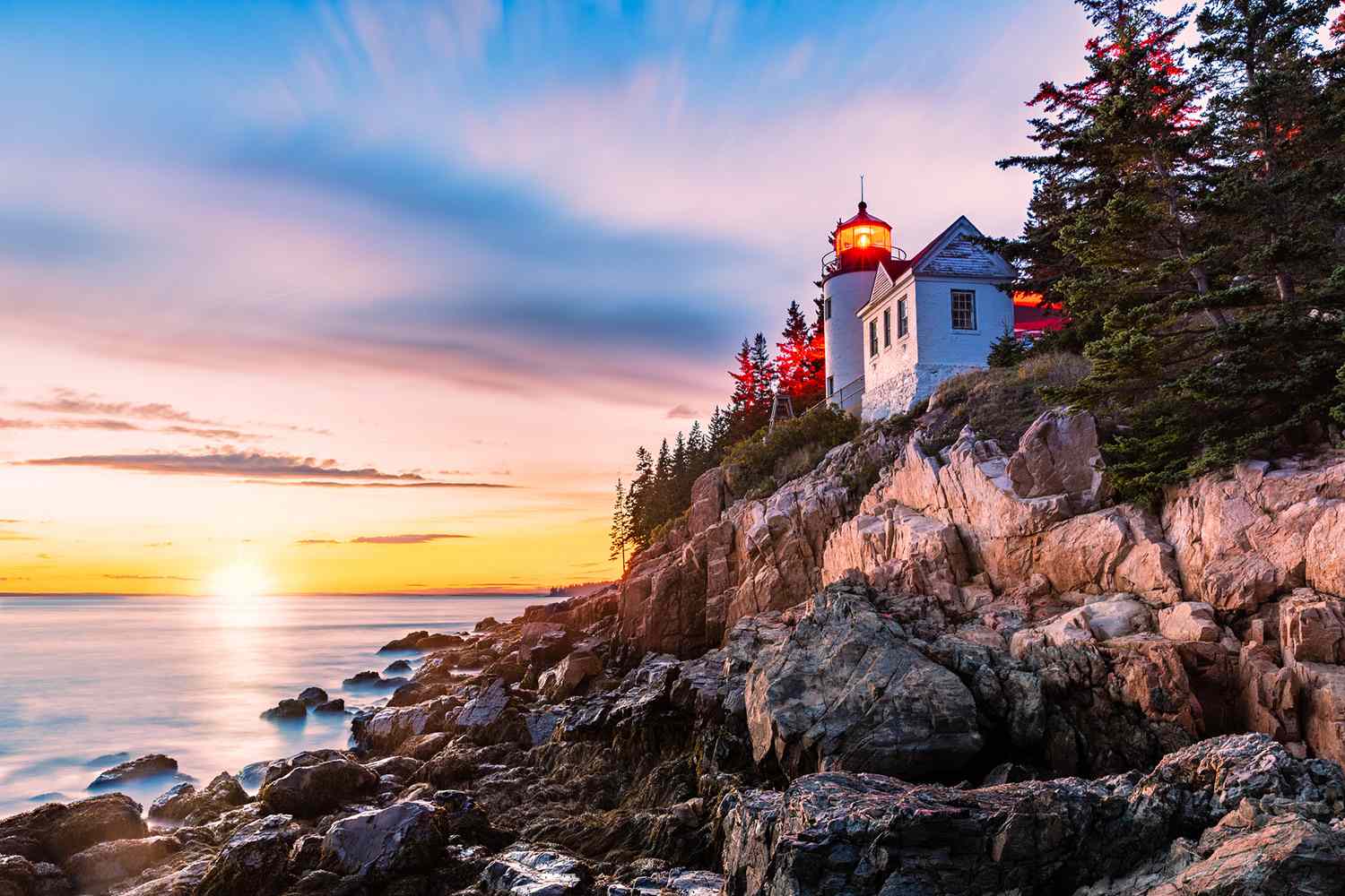 Bass Harbor Head Lighthouse perched on rocky cliffs during a colorful oceanfront sunset in Acadia National Park, Maine.