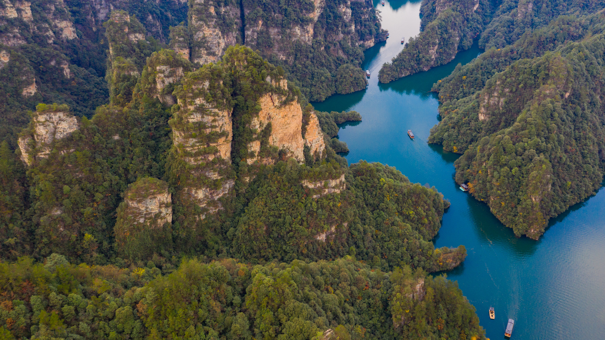 Aerial view of Baofeng Lake in Zhangjiajie National Forest Park, China, surrounded by steep forest-covered sandstone peaks and calm blue water with sightseeing boats.