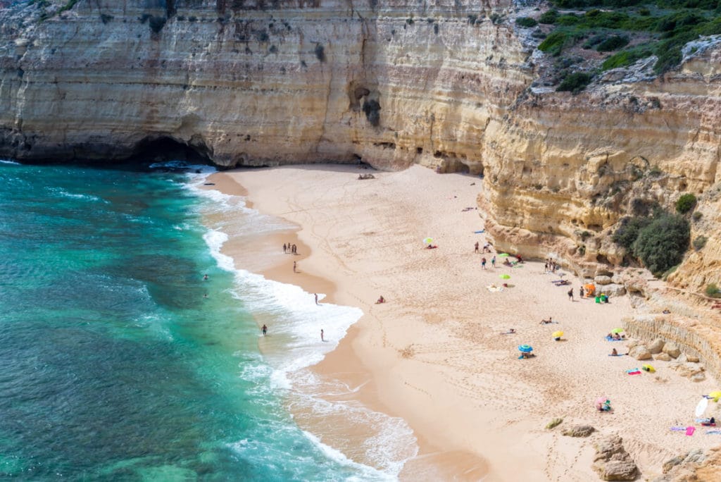 People playing on a beautiful beach in Praia do Vale de Centeanes with clear blue waters.