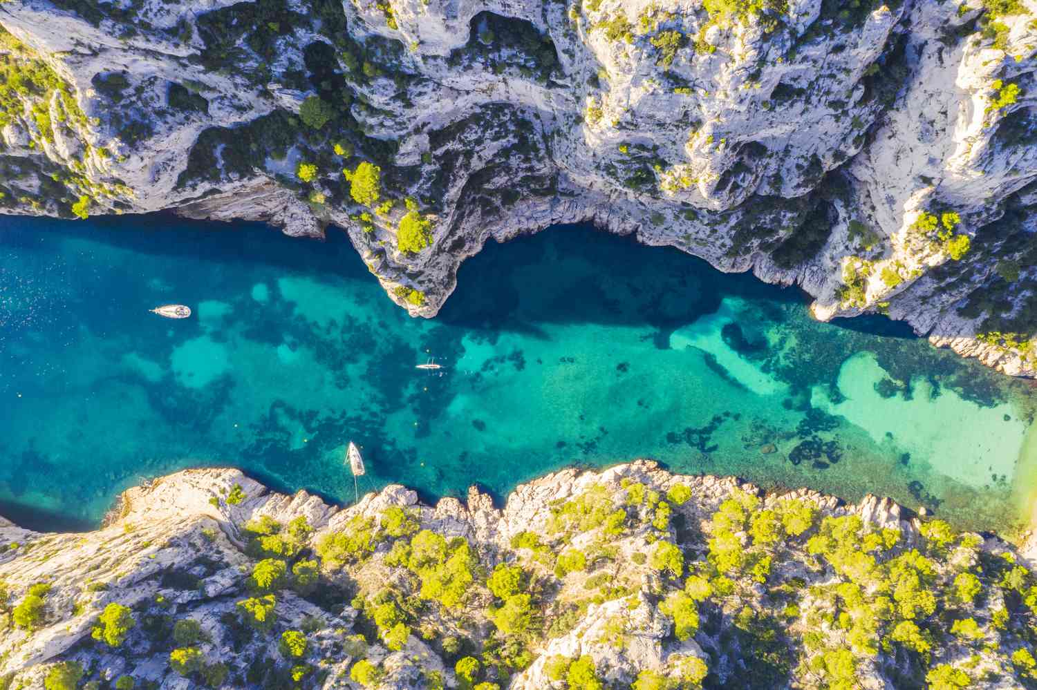 Aerial view of the Calanques with steep cliffs, clear blue waters, and boats anchored in a narrow inlet.