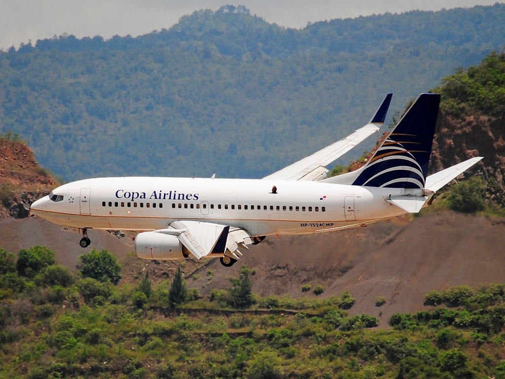 Copa Airlines Boeing 737 aircraft preparing to land against a mountainous, green landscape, with landing gear deployed and the airline's blue and gold logo visible on the tail.