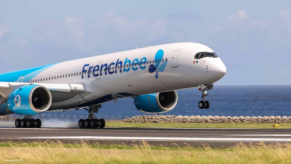 A White Airplane with blue writing that says Frenchbee on the side of it landing at the airport. 