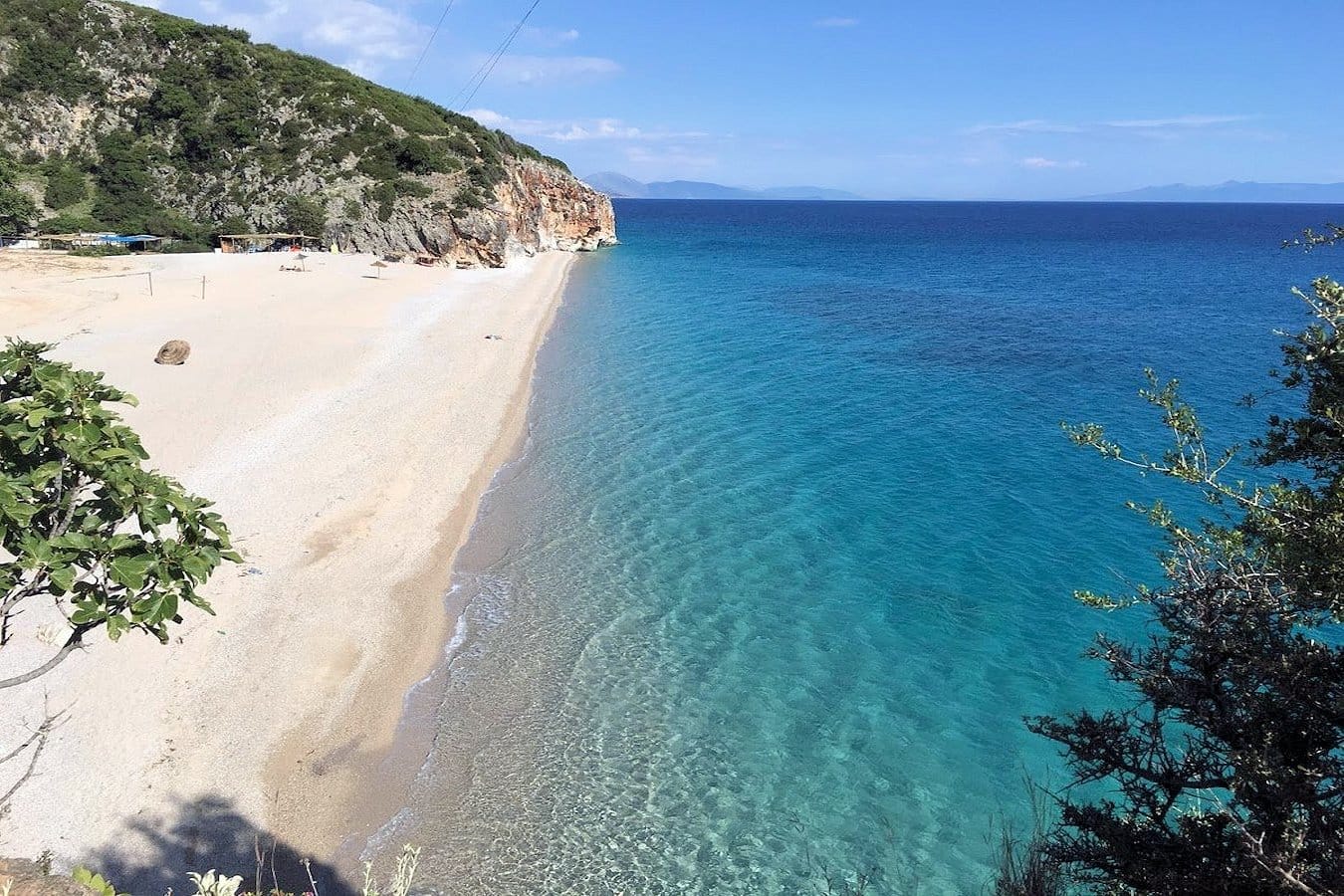 Gjipe Beach in Albania with turquoise water, dramatic cliffs, and an empty stretch of soft white sand along a quiet shoreline.