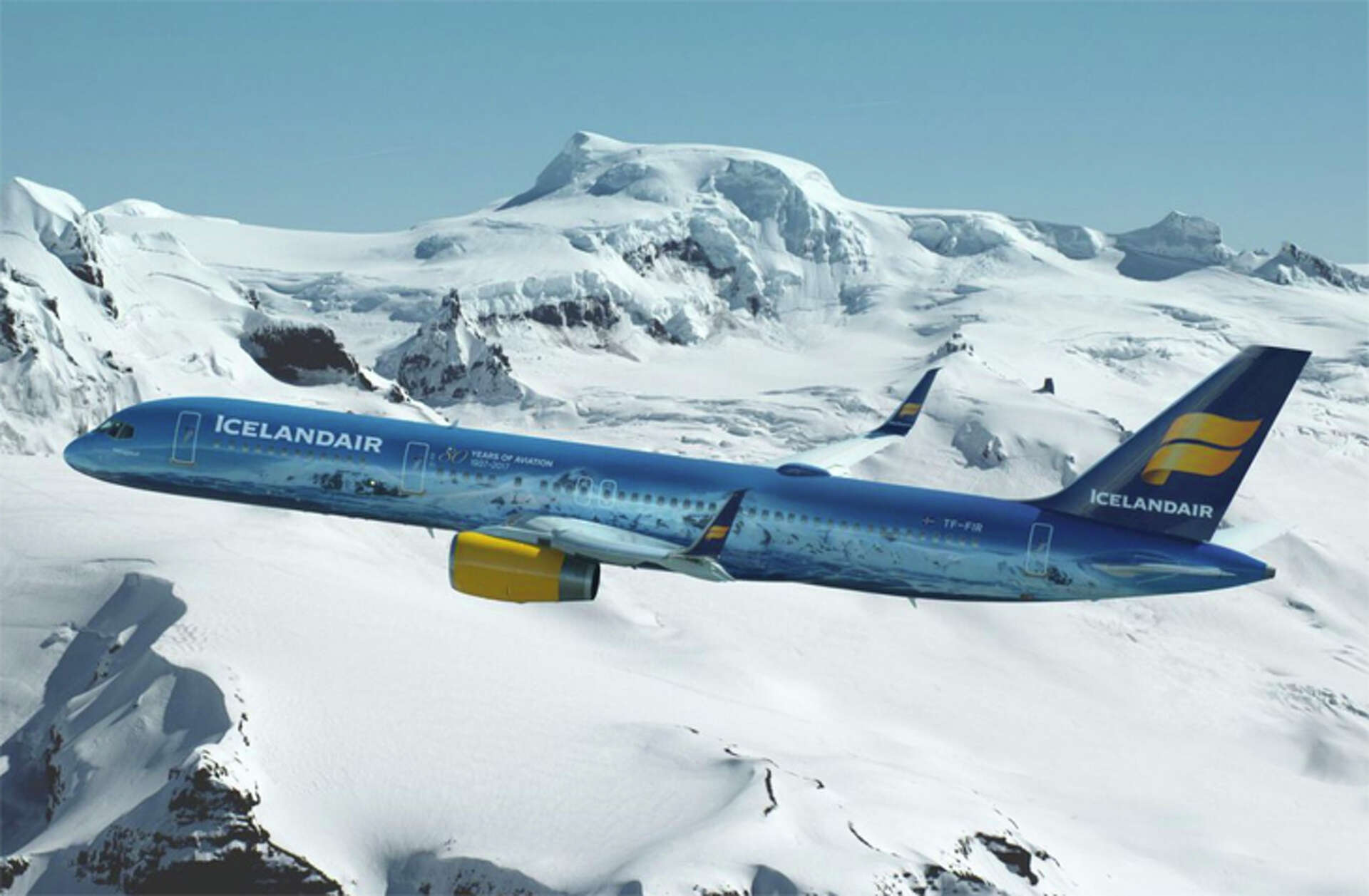 Blue Icelandair plane flying over snow covered mountains as it arrives to Iceland from Seattle. 