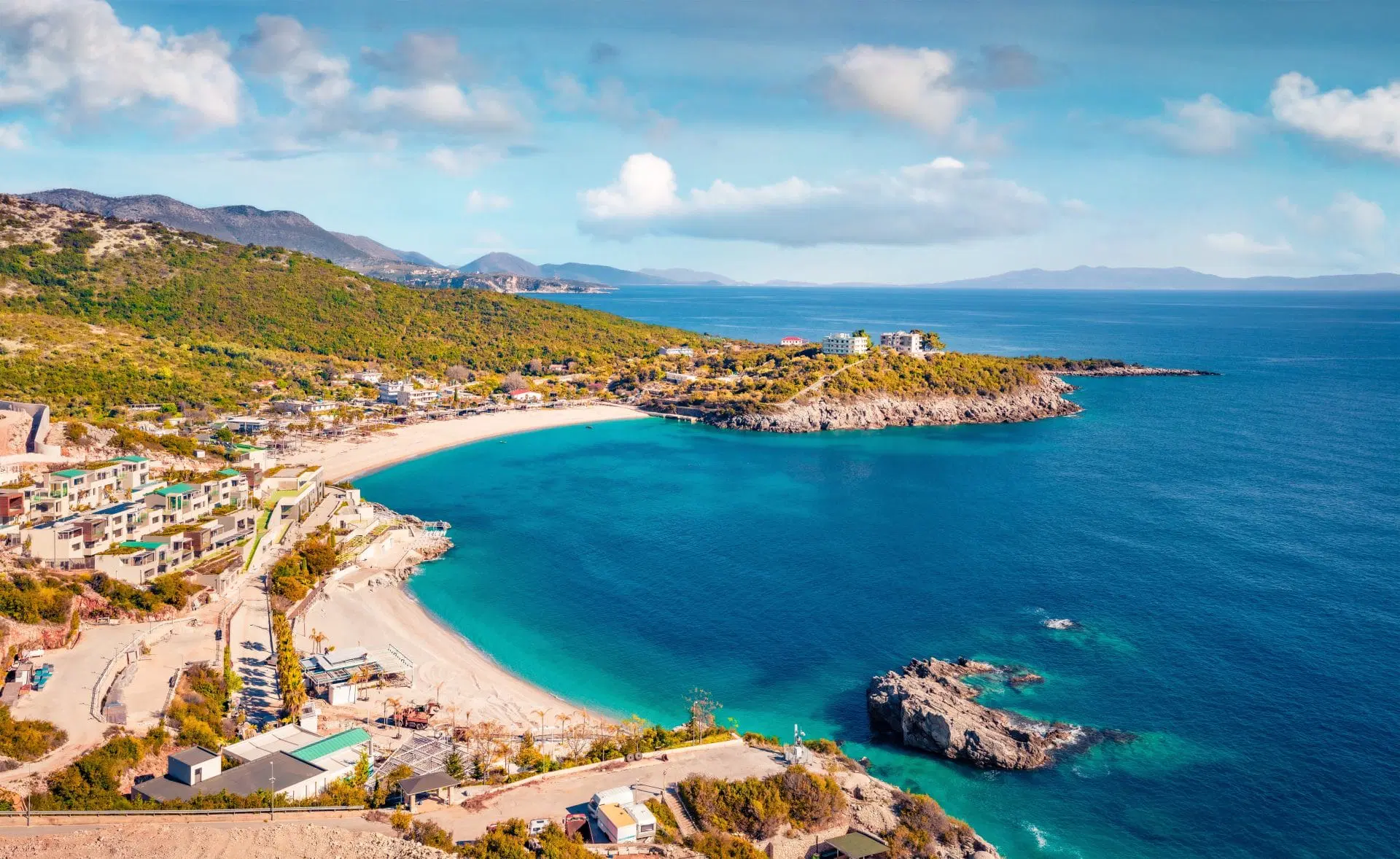 Aerial view of Jale Beach near Dhërmi, Albania, with turquoise water, sandy shores, rocky coastline, and hillside resorts.