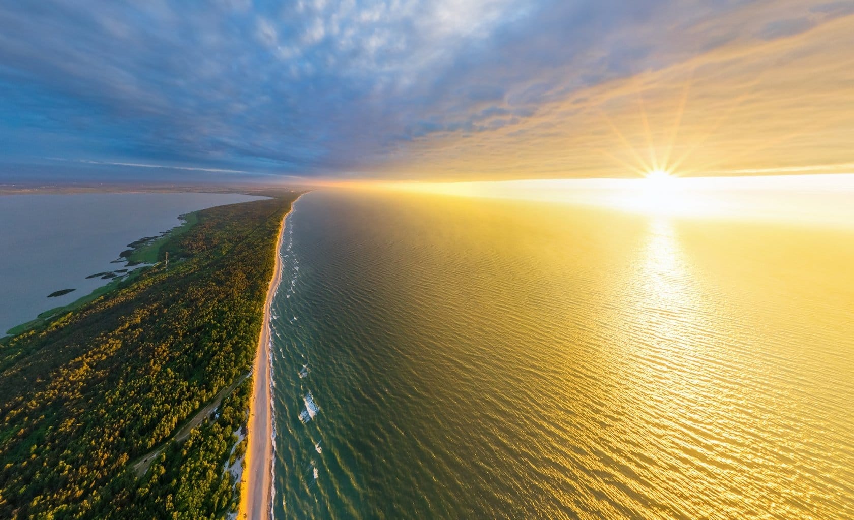 Aerial view of the Curonian Spit dividing the Baltic Sea and a lagoon at sunset in Kurshskaya Kosa National Park.