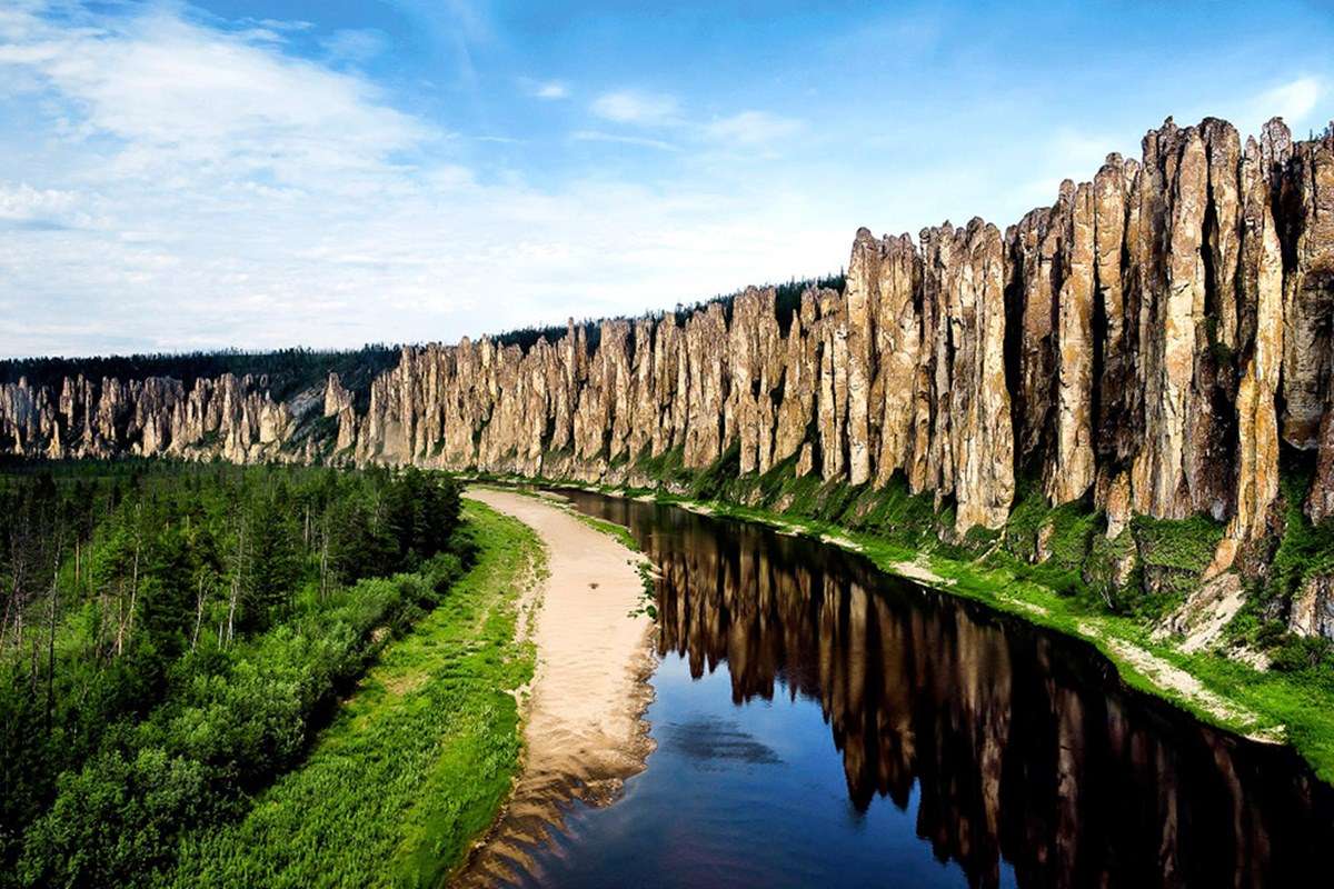 Towering stone columns rise beside a river in Lena Pillars National Park, Yakutia, framed by forest and sky.