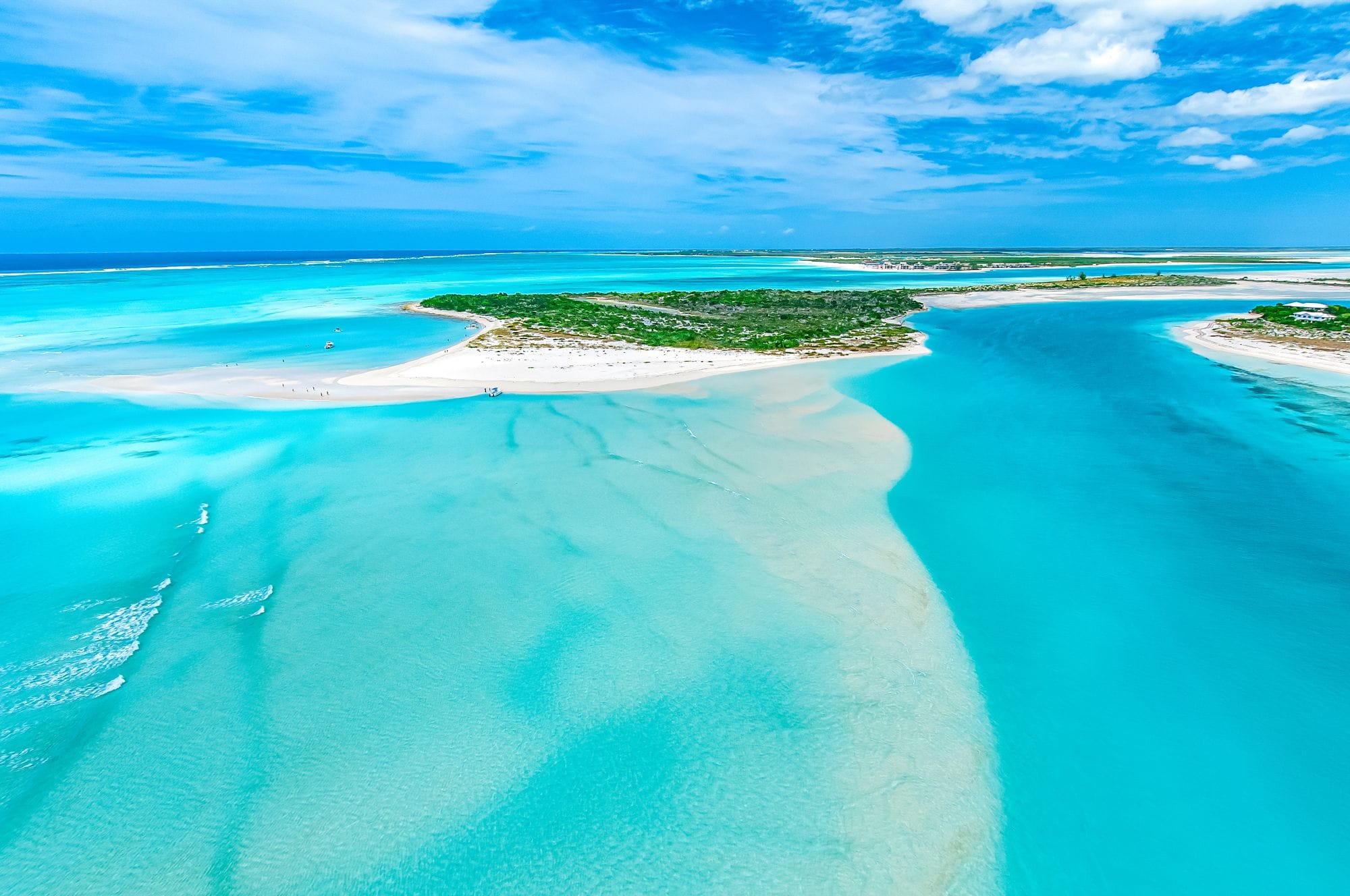 Aerial view of Little Water Cay in Turks and Caicos featuring white sandy beaches, shallow turquoise waters, and lush greenery under a partly cloudy blue sky.