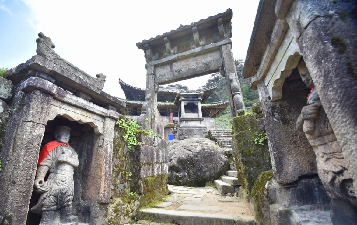 Stone pathway leading to an ancient temple complex at Mount Sanqingshan National Park in China, featuring traditional Chinese architecture, weathered statues, and moss-covered stonework.