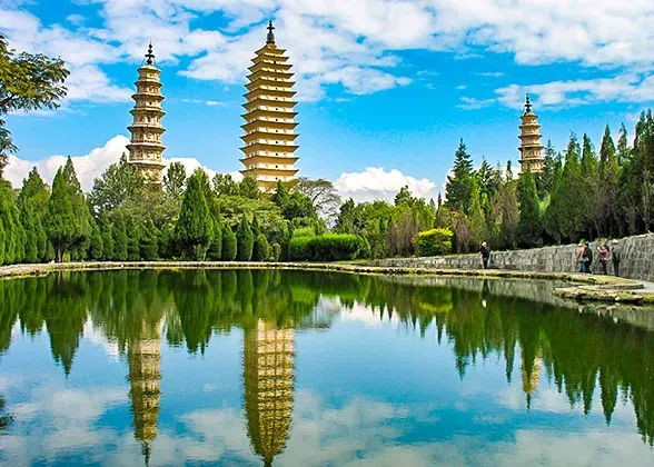 Scenic view of a traditional Chinese pavilion and arched stone bridge reflected in a tranquil lake at Potatso National Park, Yunnan, China, with snow-capped mountains rising in the background.