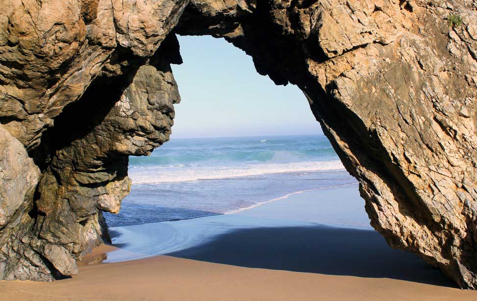 A hole through a cliff with a view of the ocean at Praia da Adraga - Portugal.