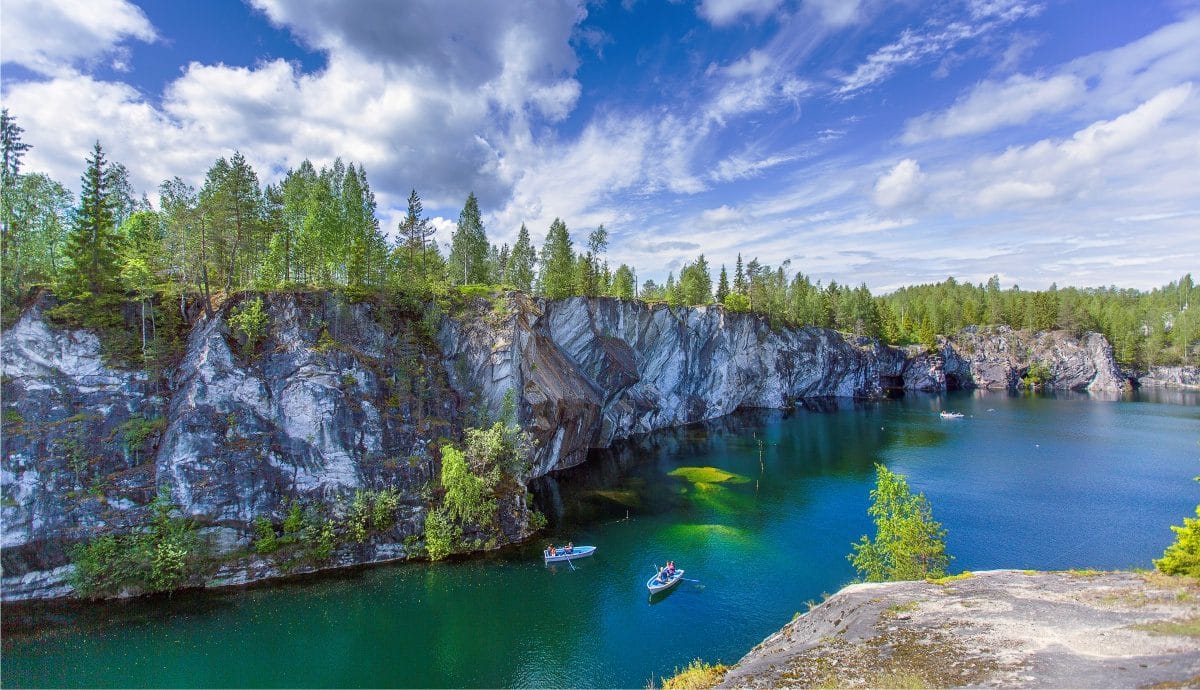 Emerald lake surrounded by marble cliffs and forest in Ruskeala Mountain Park, Karelia, with small boats on the water.