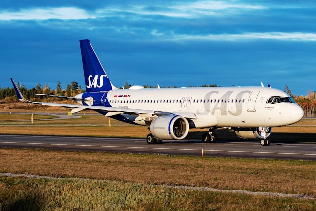 SAS Scandinavian Airlines Airbus taxiing on runway with blue sky and forest backdrop.