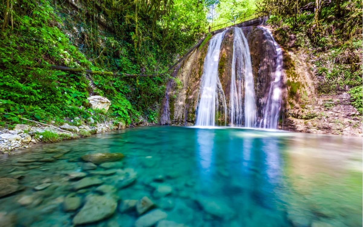 Clear turquoise pool at the base of a lush green waterfall in Sochi National Park, Western Caucasus.