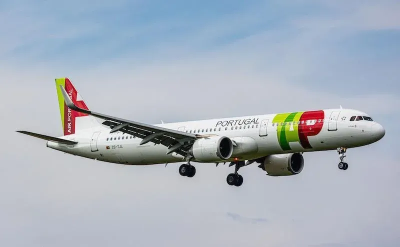 An Airplane flying with it's landing gear down and says TAP on the side of the plane in Green and Red letters.