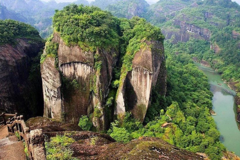 Aerial view of Wuyishan National Park in Fujian, China, featuring dramatic Danxia landform cliffs covered in green vegetation and a winding river cutting through the mountainous landscape.