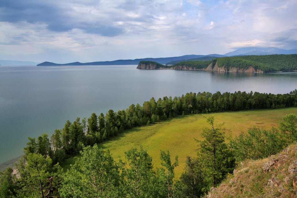 Wide view of a calm lake bordered by green hills and forest in Zabaykalsky National Park, Eastern Siberia.