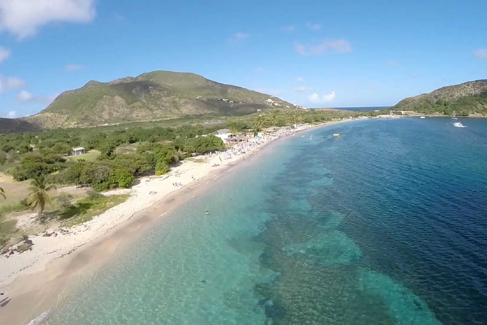 Cockleshell Bay Beach ariel view with white sandy beach, clear blue waters and a mountain in the background.