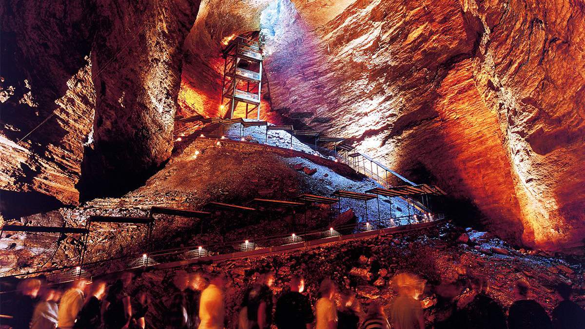 A huge cave with people standing inside of it looking up at a hole with the sun shining through it at Marvel Cave inside Silver Dollar City Branson Missouri.